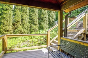 A wooden deck with a metal railing overlooking a forested area.