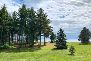 A grassy area with tall trees and a view of a body of water. - Waterfront Whitefish Lake Home w/ Dock! (Pine River)
