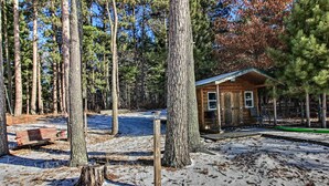A cabin surrounded by tall pine trees, a wooden deck, and a snow-covered ground. - Waterfront Whitefish Lake Home w/ Dock! (Pine River)