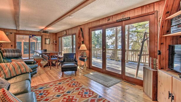 A cozy cabin interior with a wooden interior, a large sliding glass door leading to a deck, a leather sofa, and a television on a wooden cabinet. - Waterfront Whitefish Lake Home w/ Dock! (Pine River)