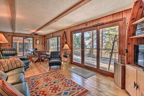 A cozy cabin interior with a wooden interior, a large sliding glass door leading to a deck, a leather sofa, and a television on a wooden cabinet.