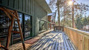 A wooden deck with a metal railing, large windows, and a view of trees. - Waterfront Whitefish Lake Home w/ Dock! (Pine River)