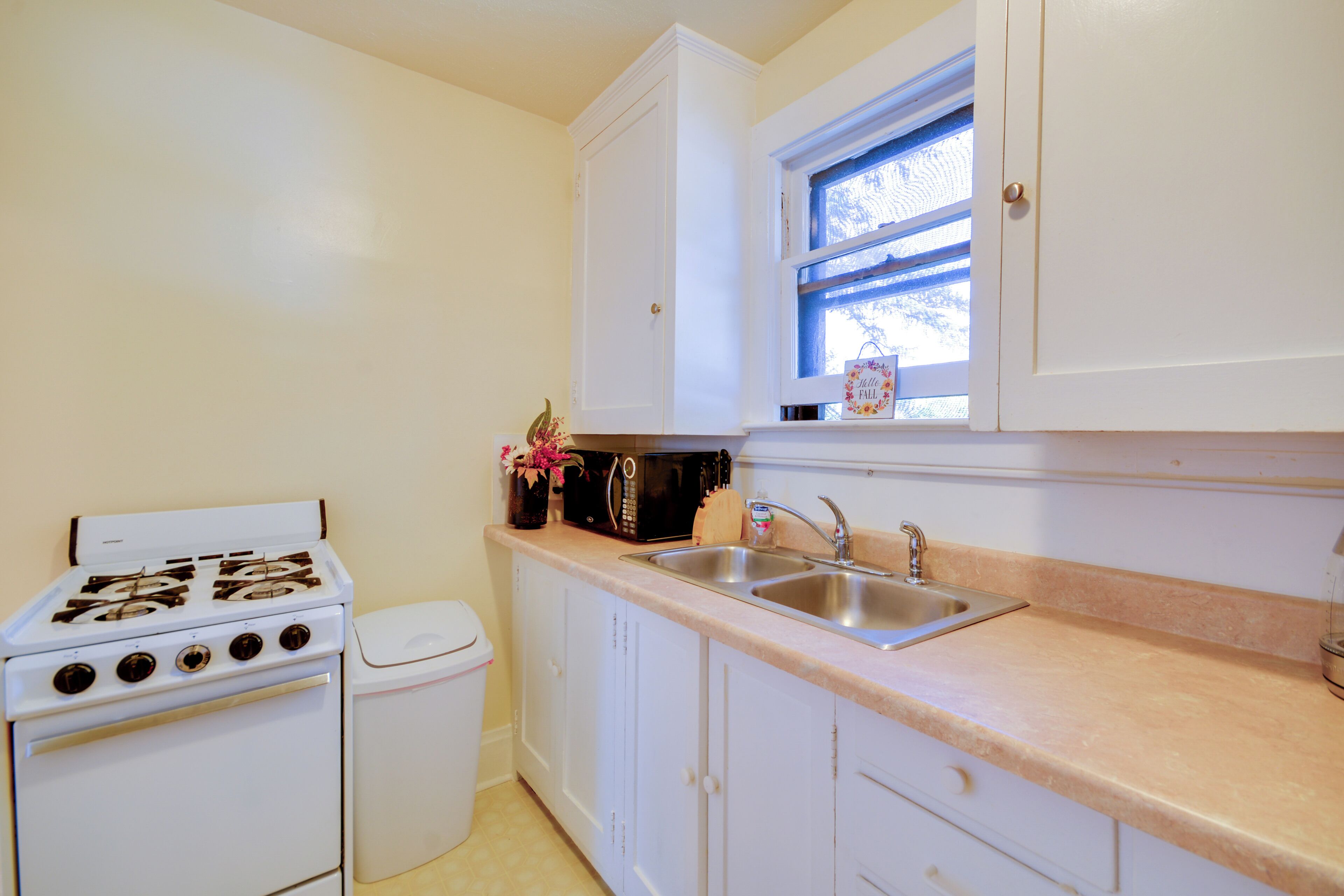 A kitchen with white cabinets, a stove, a sink, and a window with a view.