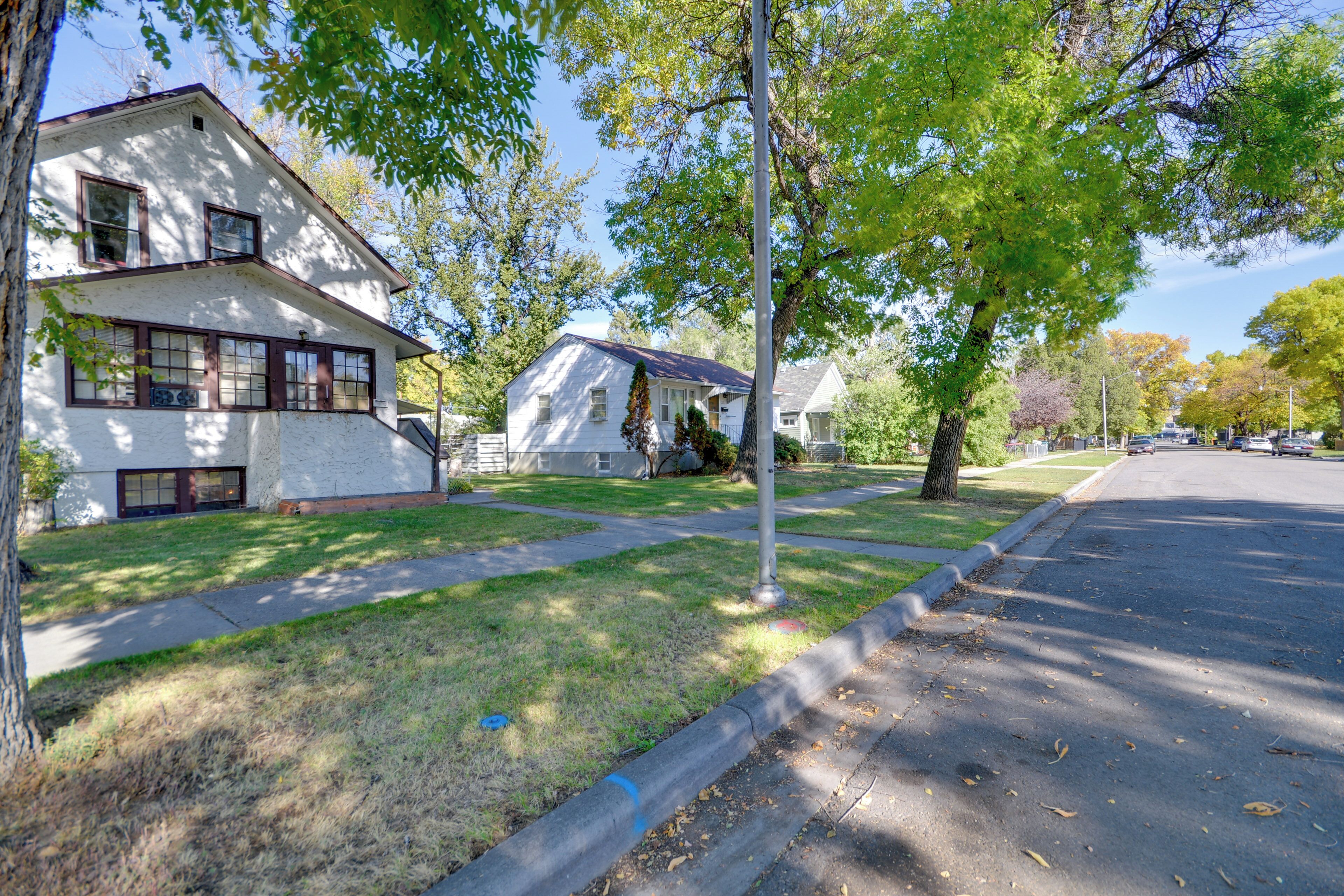 A residential street with houses, a sidewalk, and a tree-lined road.