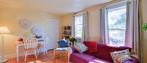A cozy living room with a sofa, a dining table with chairs, a lamp, and a bookshelf.