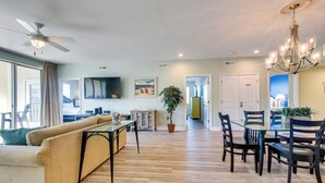 A spacious living room with a sofa, dining table, chairs, and a chandelier. - Walk to Shore: Roomy Condo in North Myrtle Beach! (North Myrtle Beach)