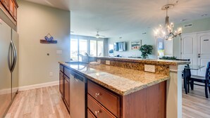 A modern kitchen with granite countertops, wooden cabinets, and a central island. - Walk to Shore: Roomy Condo in North Myrtle Beach! (North Myrtle Beach)