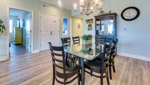 A dining area with a glass table, dark chairs, a chandelier, and a clock on the wall. - Walk to Shore: Roomy Condo in North Myrtle Beach! (North Myrtle Beach)