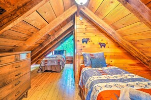 A cozy attic bedroom with wooden walls and a sloped ceiling, featuring a bed, a dresser, and a window with a view of greenery outside. - Homey Sevierville Getaway w/ Hot Tub & Deck! (Sevierville)