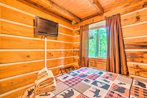 Una camera da albergo con arredamento in legno, una televisione a parete, una coperta con stampe di animali sul letto e una finestra con tende.