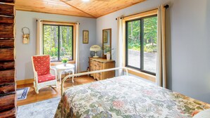 A room with a bed, a chair, a table, and a window with a view of trees. - Serene Wilderness Acres Retreat on Bear Lake (Mc Grath)