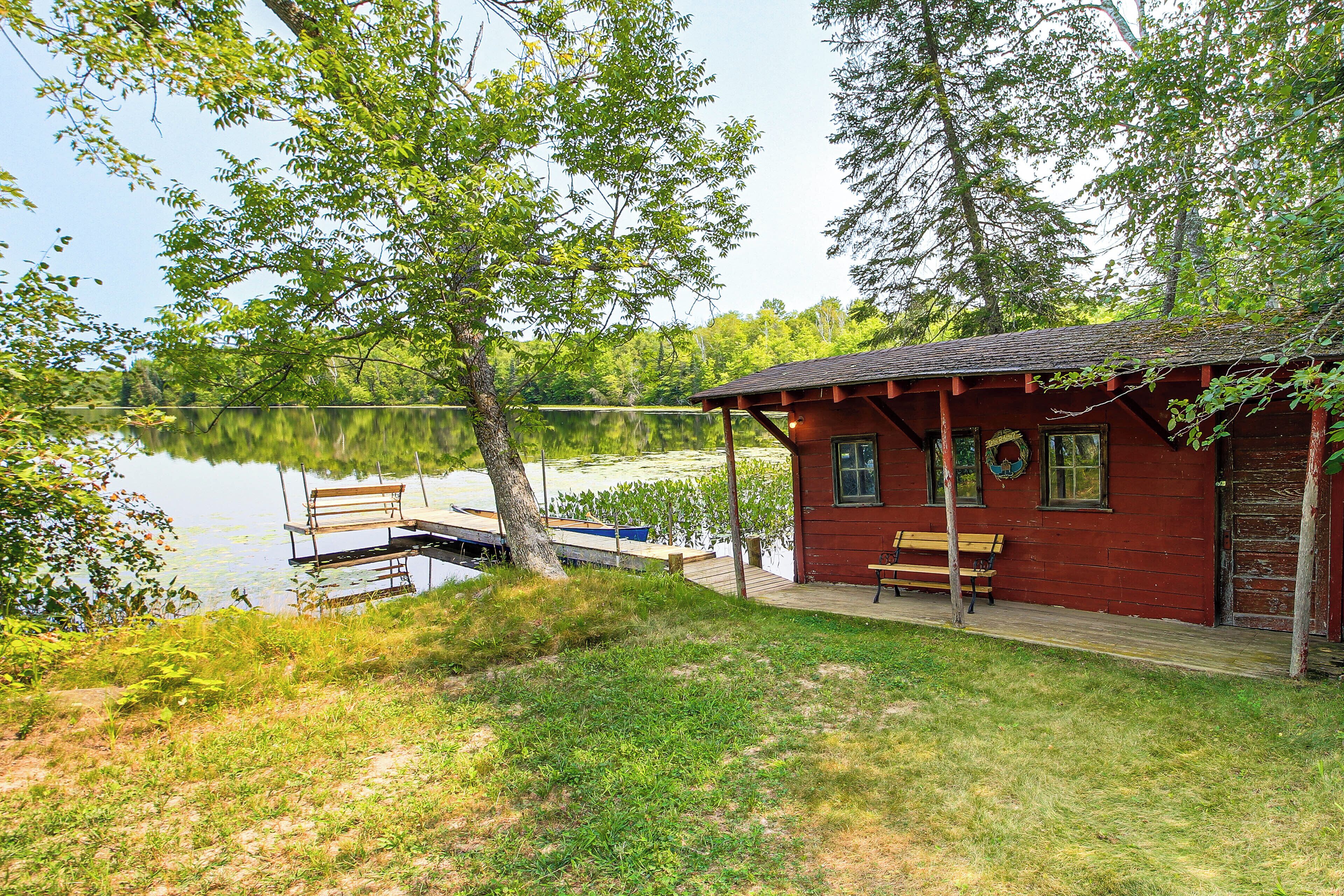 Una cabaña junto al lago con muelle, banco y pequeño porche.