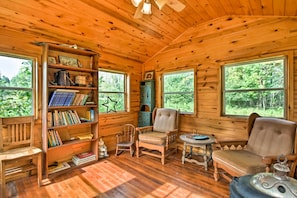 A wooden cabin interior with a bookshelf, two rocking chairs, a sofa, and a table.