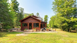A wooden cabin with a porch, outdoor seating, and a grill area. - Serene Wilderness Acres Retreat on Bear Lake (Mc Grath)