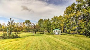 A small, single-story house with a green roof, surrounded by a well-maintained lawn and trees. - Serene Wilderness Acres Retreat on Bear Lake (Mc Grath)