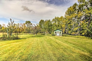 A small, single-story house with a green roof, surrounded by a well-maintained lawn and trees. - Wilderness Acres Retreat on Bear Lake! (Mc Grath)