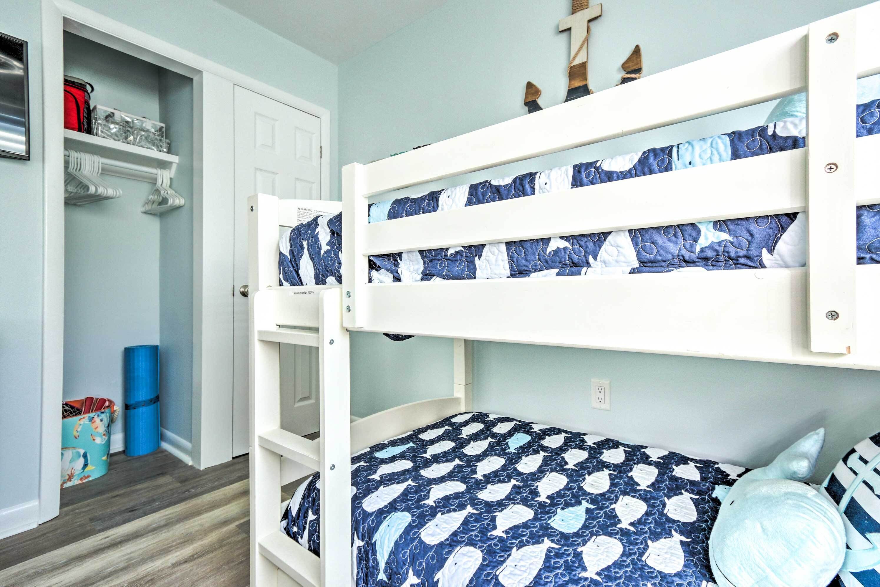 A bunk bed with a blue and white patterned bedspread, a white door, a shelf with various items, and a blue yoga mat on the floor.