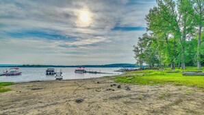 A beach with boats, a sandy shore, and a forested area. - Lakefront Gloversville Home w/ Beach + Dock! (Gloversville)
