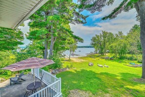 A covered patio with a table and chairs, overlooking a grassy area with boats and a dock by a lake. - Lakefront Gloversville Home w/ Beach + Dock! (Gloversville)