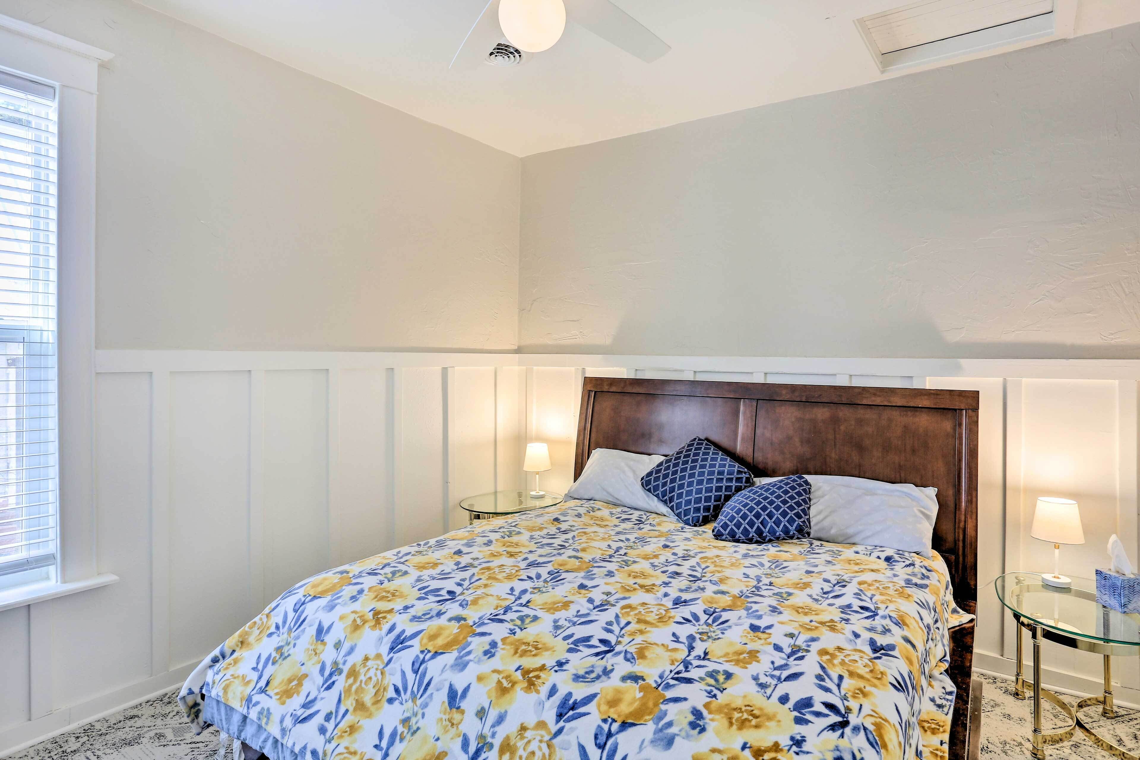 A bedroom with a large bed, a wooden headboard, two bedside tables with lamps, and a window with blinds.