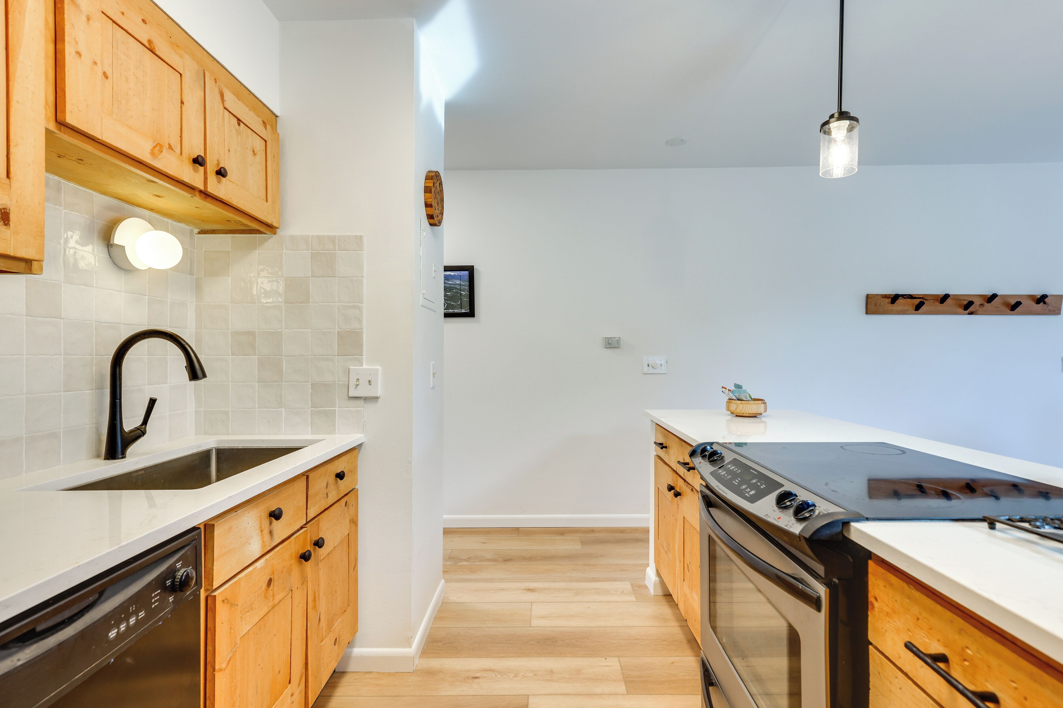 Une cuisine moderne avec des meubles en bois, un lave-vaisselle, un four et un luminaire suspendu.