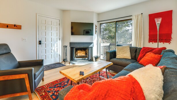 A modern living room with a fireplace, a sofa, a coffee table, and a large window with curtains. - Walk to Winter Park Bus From Fraser Condo! (Fraser)