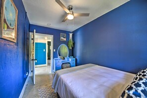 Une chambre à coucher comprenant un lit, une commode avec un miroir, un ventilateur de plafond et une porte donnant sur une autre pièce.