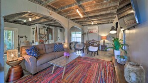 A spacious living area with a sofa, coffee table, and chairs, featuring exposed beams and a colorful rug.