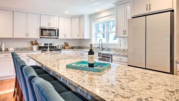 A modern kitchen with white cabinets, a large island with a marble countertop, and a built-in microwave.