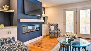 A modern living room with a fireplace, a sofa, a patterned armchair, and a glass coffee table with flowers.