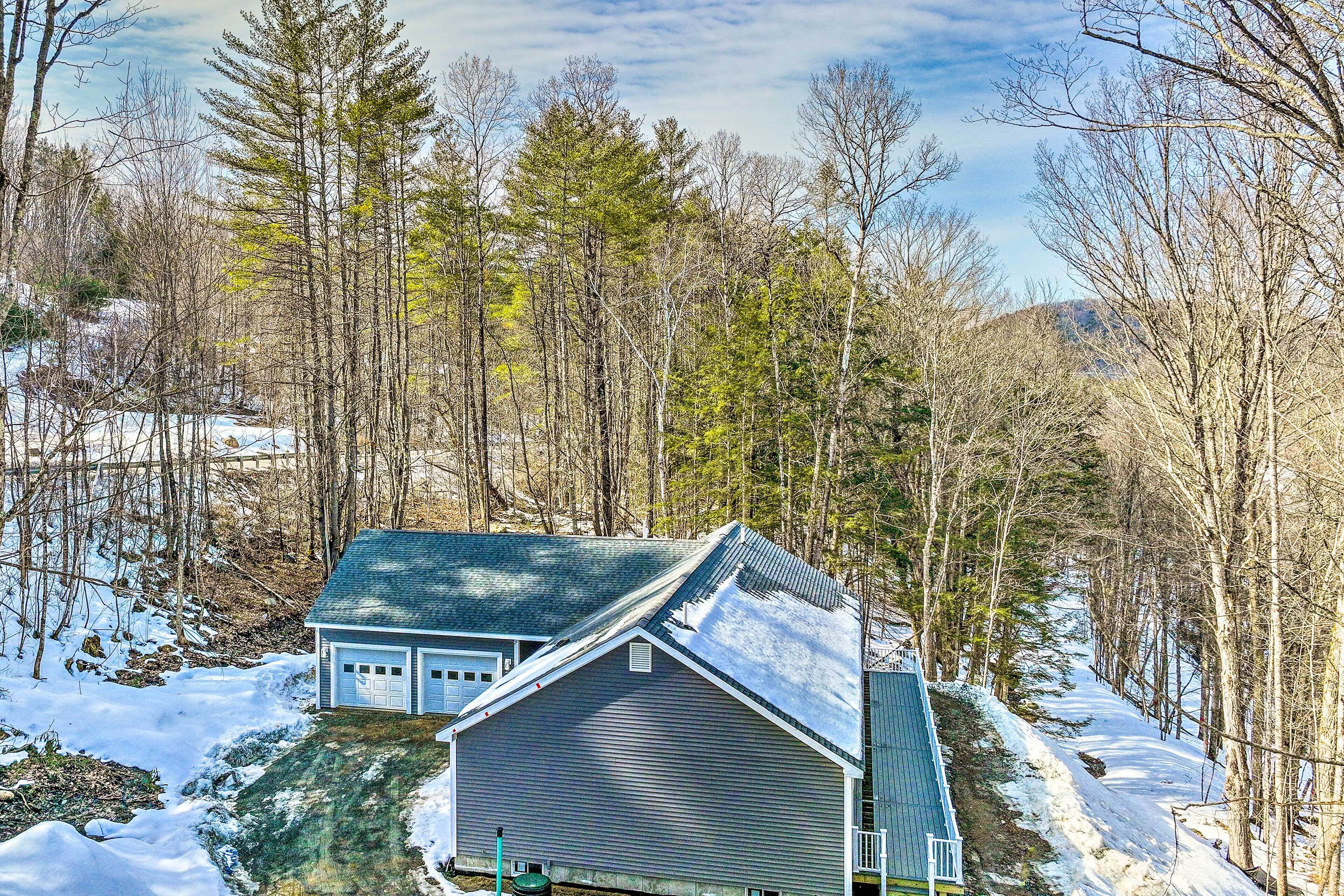 A two-story house with a gabled roof, surrounded by a forested area with snow on the ground.
