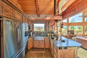 A spacious kitchen with wooden cabinets, a stainless steel refrigerator, and a large island with a sink. - Stunning Driggs Retreat w/ Private Hot Tub & Pond! (Driggs)