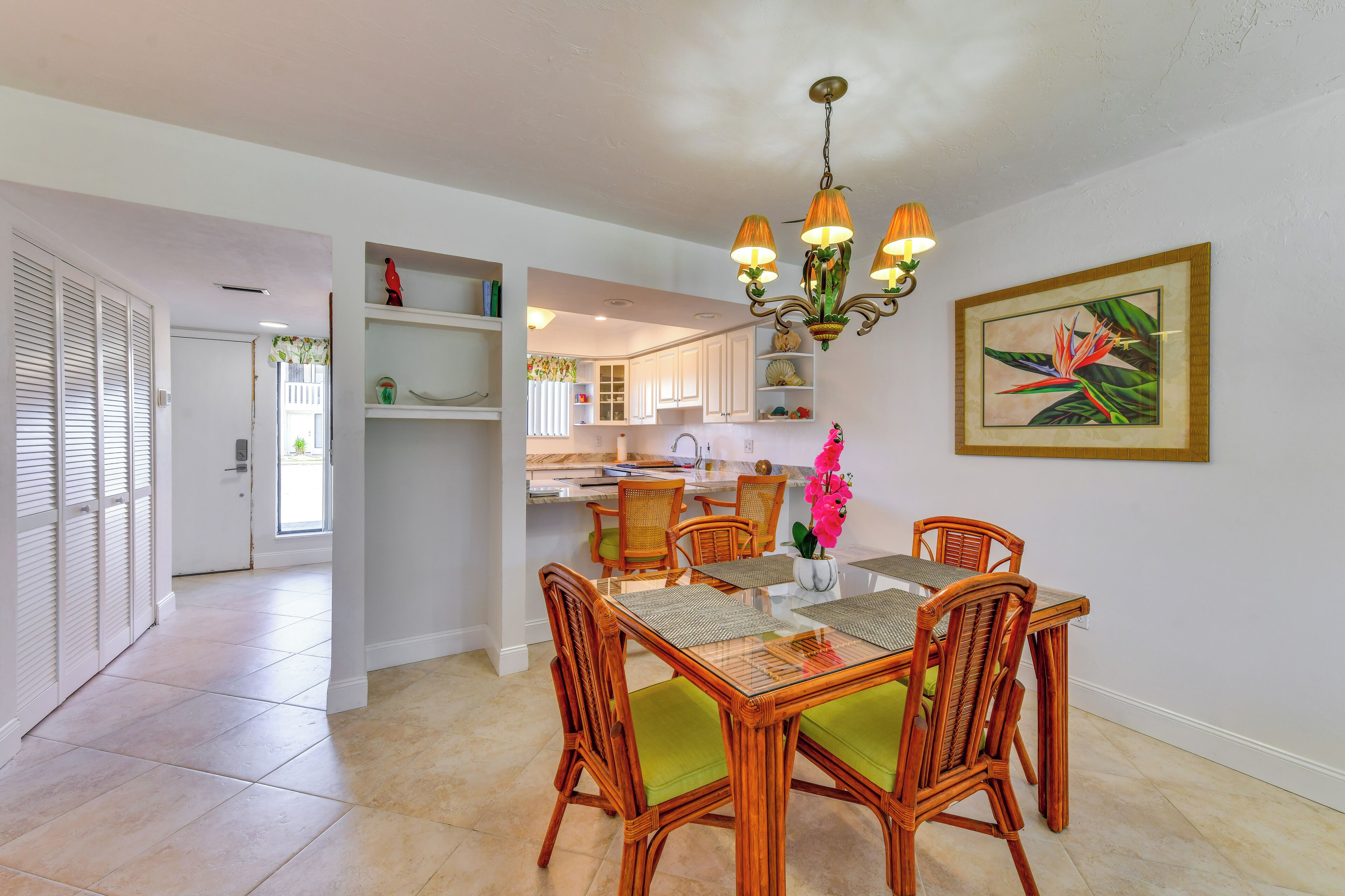 A dining area with wicker chairs and a glass table, a kitchen in the background, and a ceiling light fixture.