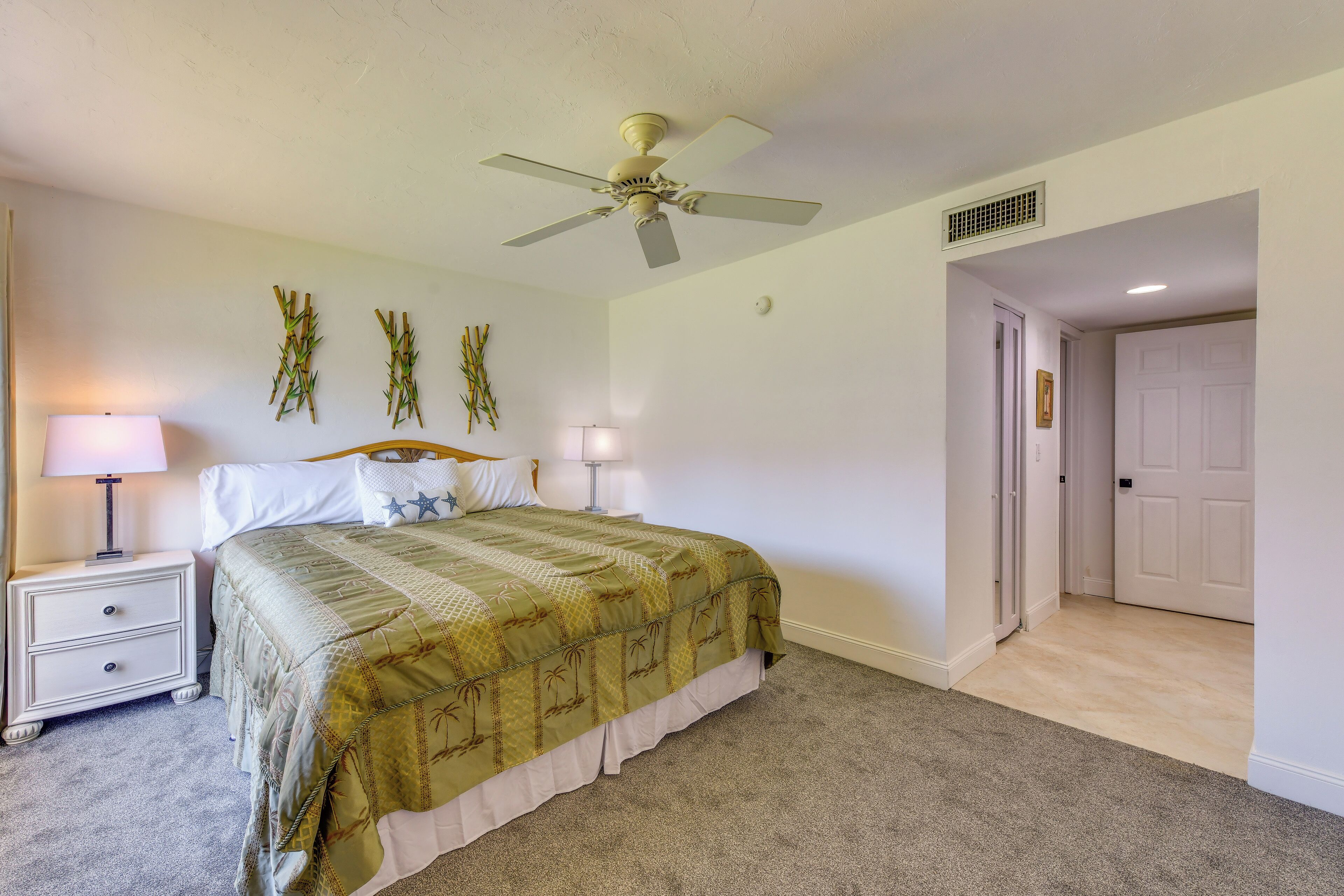 A bedroom with a bed, nightstands, a ceiling fan, and a door.
