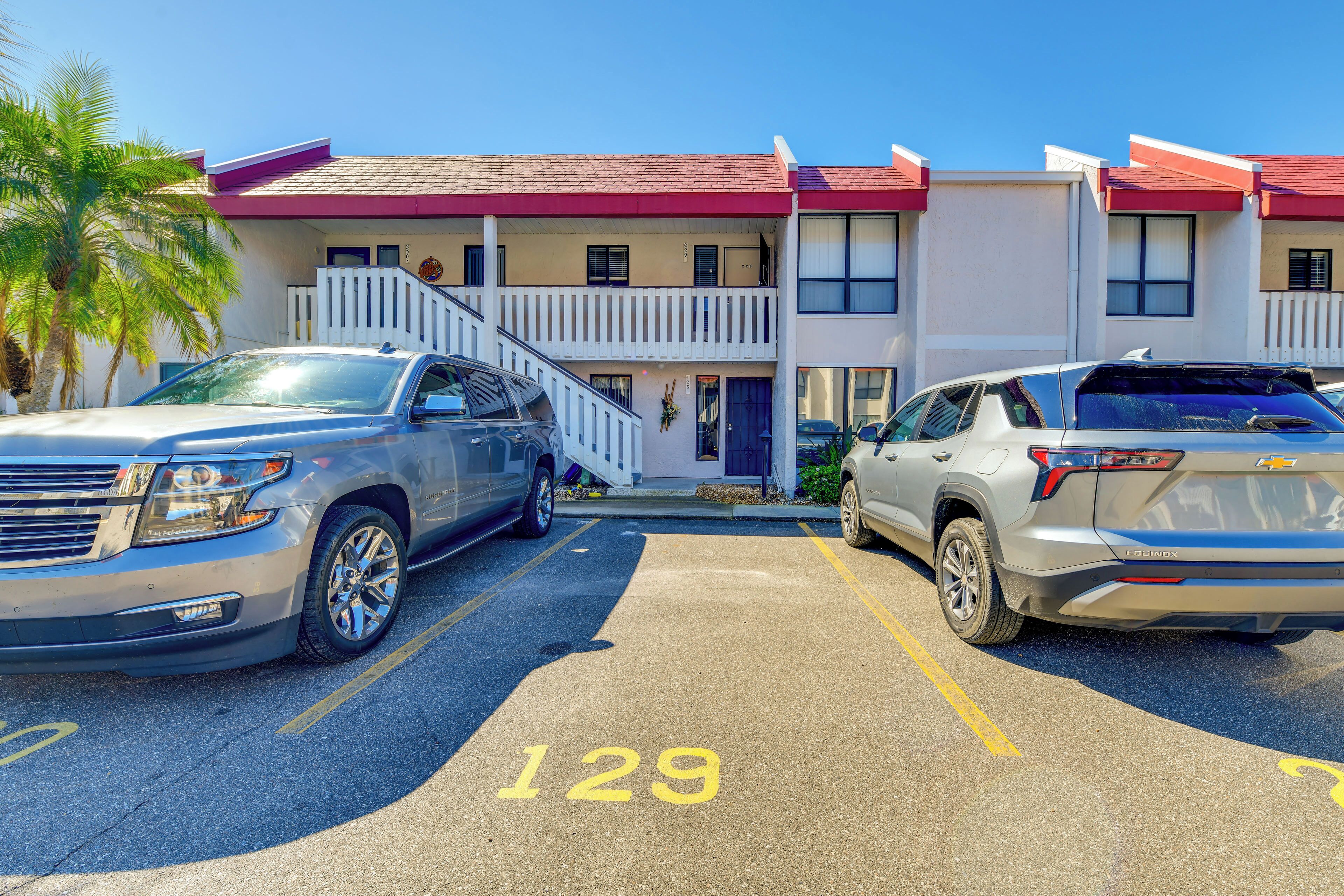A parking lot with two SUVs, a building with a red roof, and a white fence.