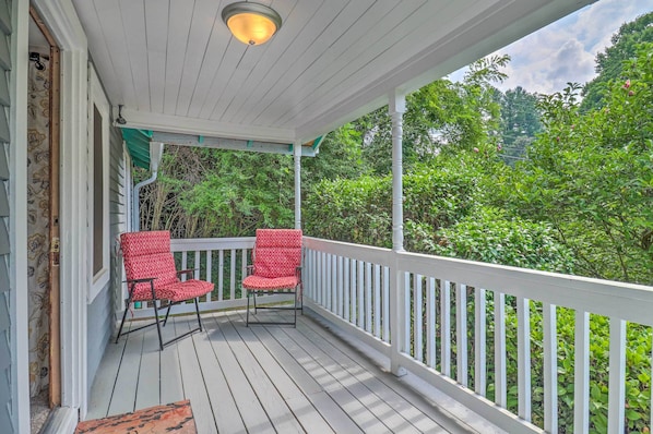 A covered porch with two red chairs, white railings, and a view of lush greenery.