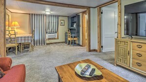 A room with a wooden table, a red sofa, a TV, a wooden cabinet, and a desk with a chair. - Near Hiking + Dining: Dtwn Sylva Cottage! (Sylva)