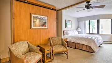 A hotel room with a bed, two armchairs, a small table, and a ceiling fan.