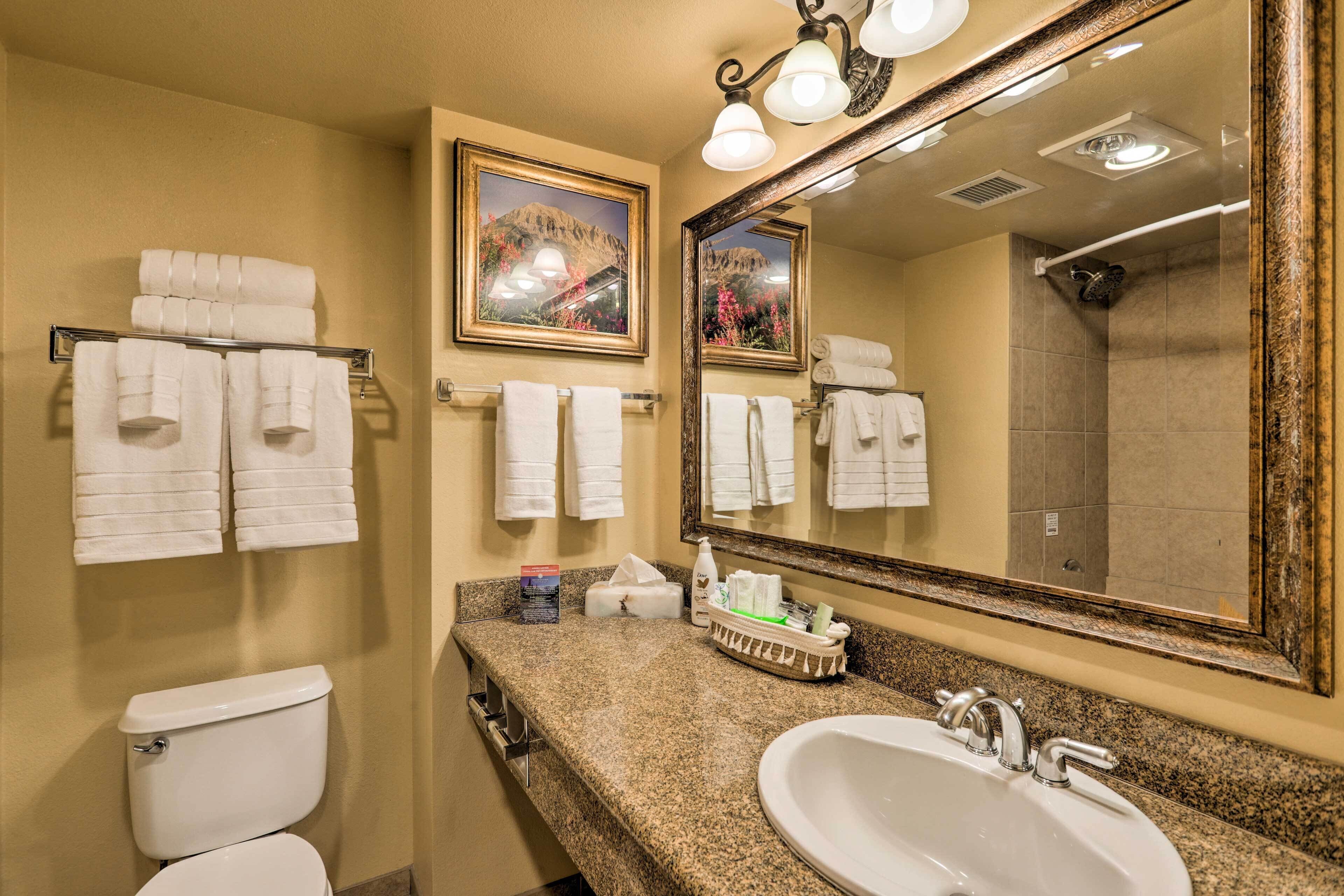 A bathroom with a toilet, sink, and shower. There are towels hanging on the wall and a large mirror above the sink.