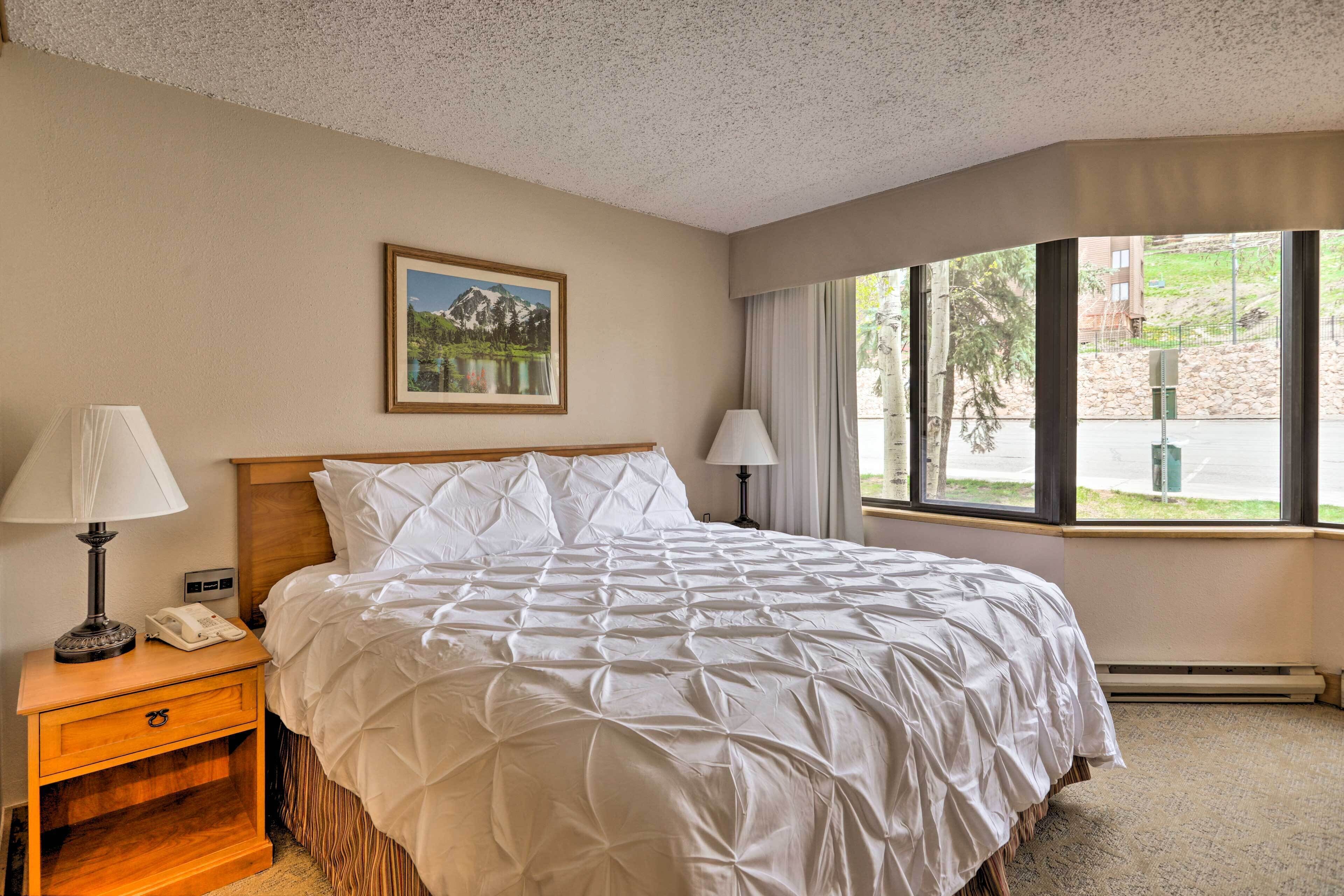 A hotel room with a large bed, two bedside lamps, a nightstand, a framed picture on the wall, and a window with a view of the outdoors.