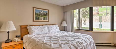 A hotel room with a large bed, two bedside lamps, a nightstand, a framed picture on the wall, and a window with a view of the outdoors.