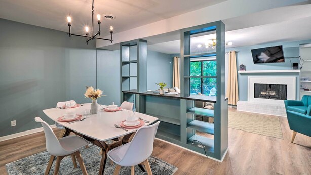 A modern dining area with a white table, two white chairs, a chandelier, and a view of a living room with a fireplace. - Stylish Durham Townhome < 5 Mi to Downtown! (Durham)