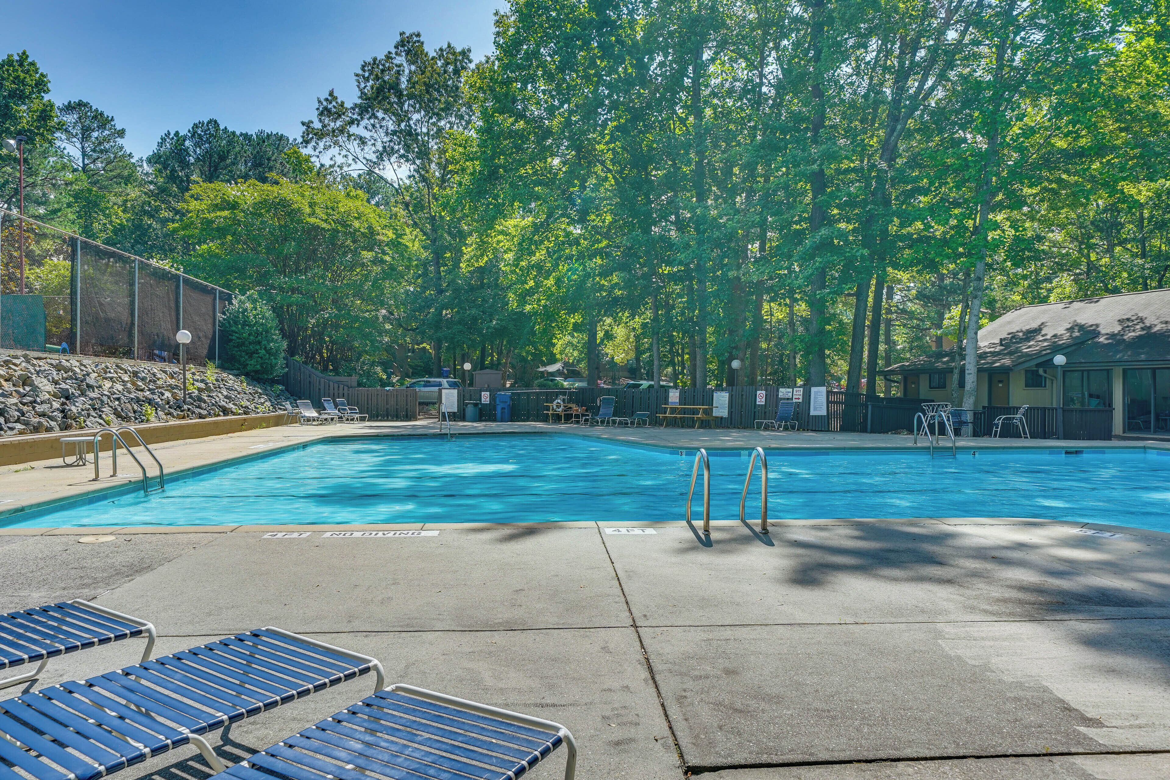 A swimming pool with lounge chairs, a fenced area, and trees in the background.