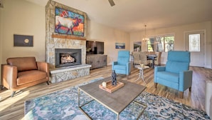 A living room with a stone fireplace, blue armchairs, a brown leather sofa, and a ceiling fan. - Beautiful Whittier Condo w/ Deck + Mtn Views! (Whittier)