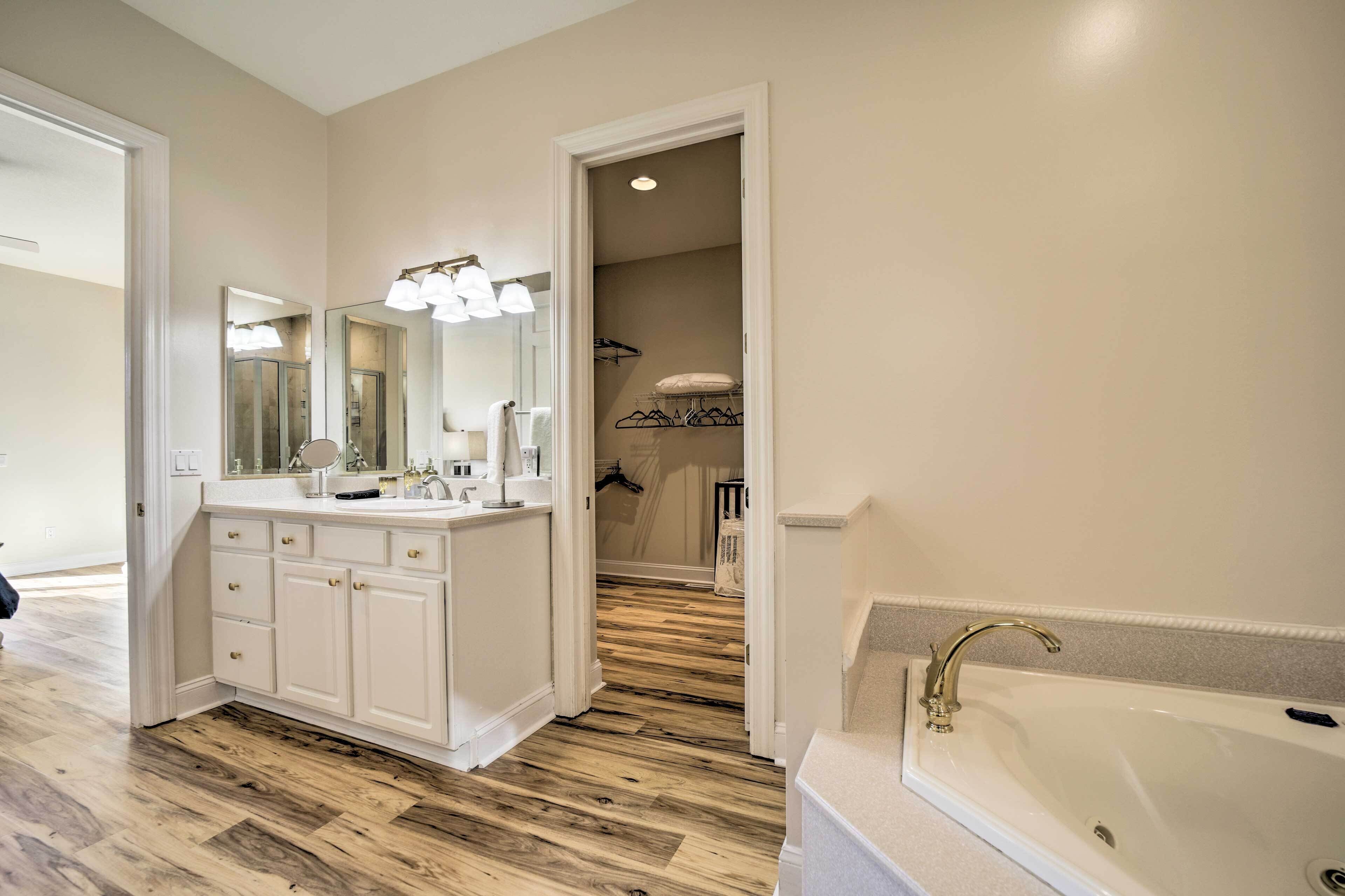 A bathroom with a double sink vanity, a bathtub, and a walk-in closet with a hanging rack.