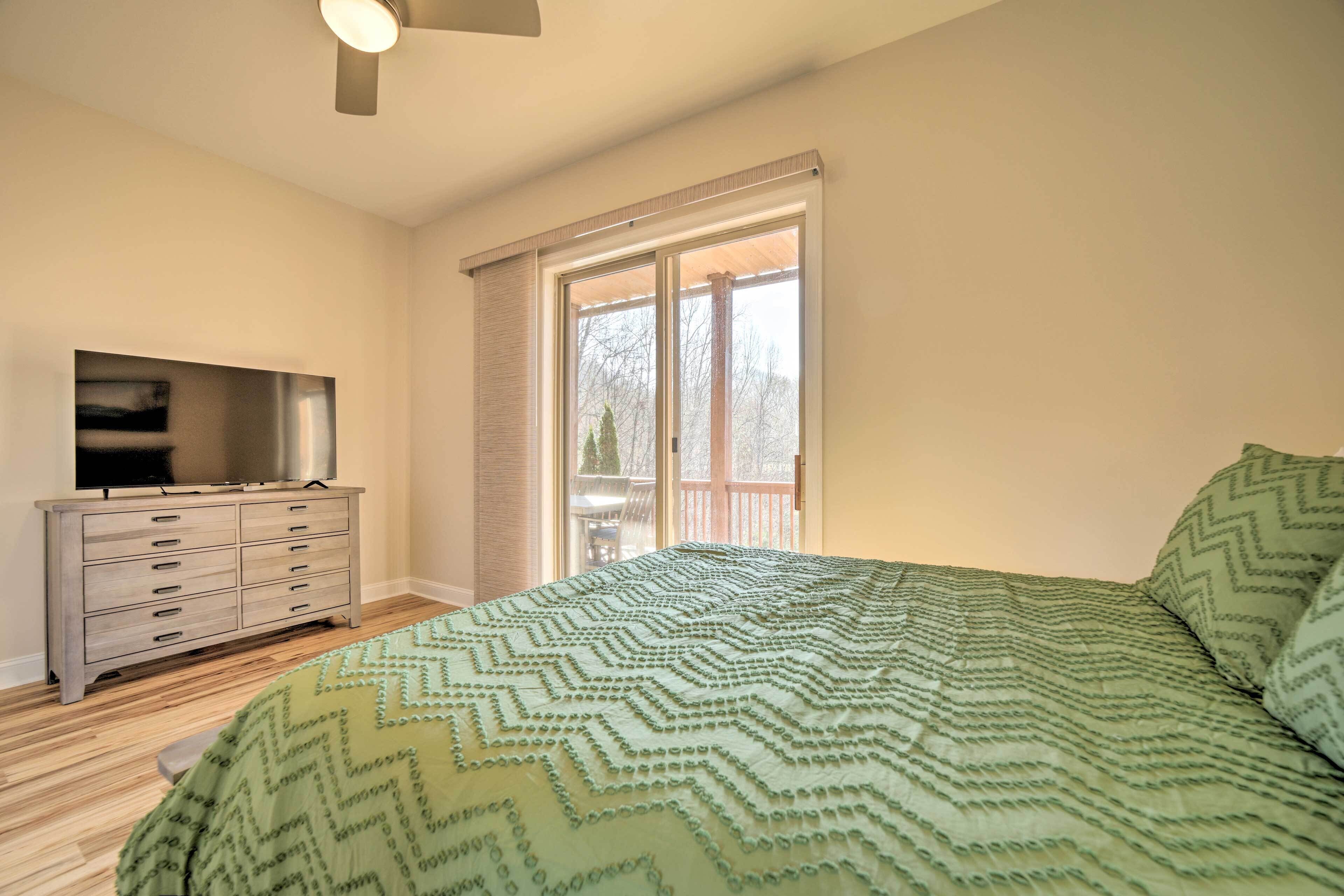 A bedroom with a bed, a dresser, a television, and a window with a view of trees.