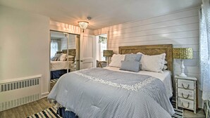 Une chambre à coucher avec un grand lit, une tête de lit en bois, un miroir, une table de chevet avec une lampe et une fenêtre avec des rideaux.