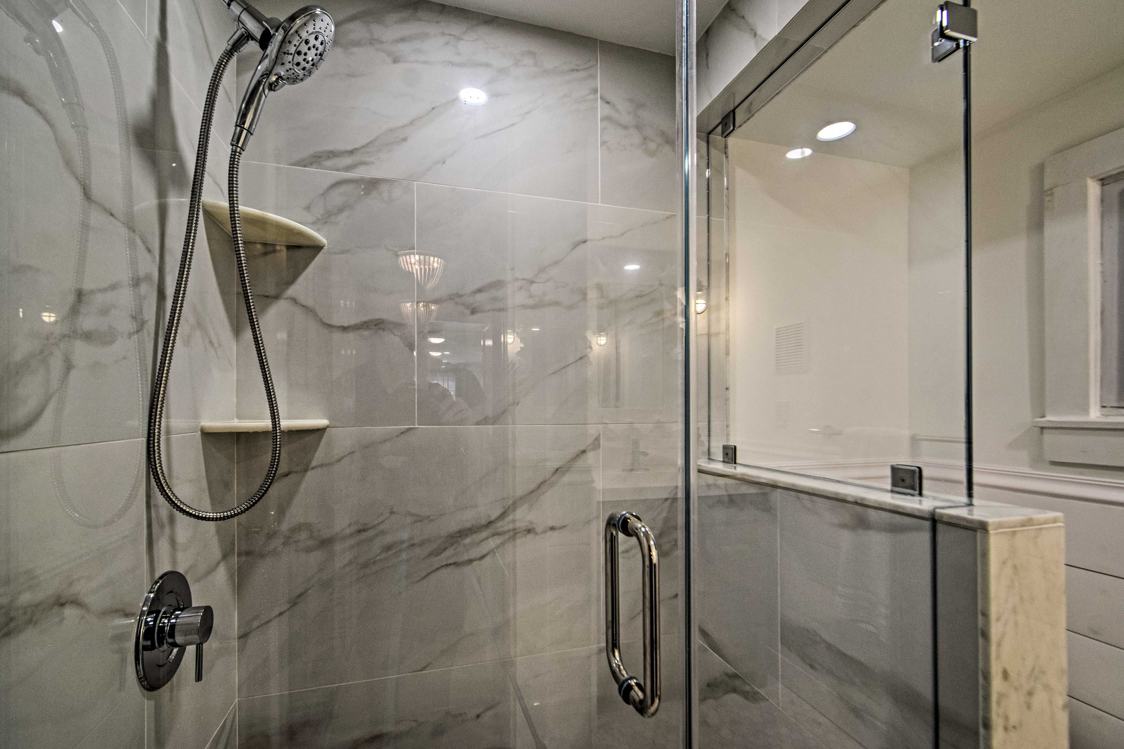 A modern bathroom with a glass shower enclosure, marble tiles, and a handheld showerhead.