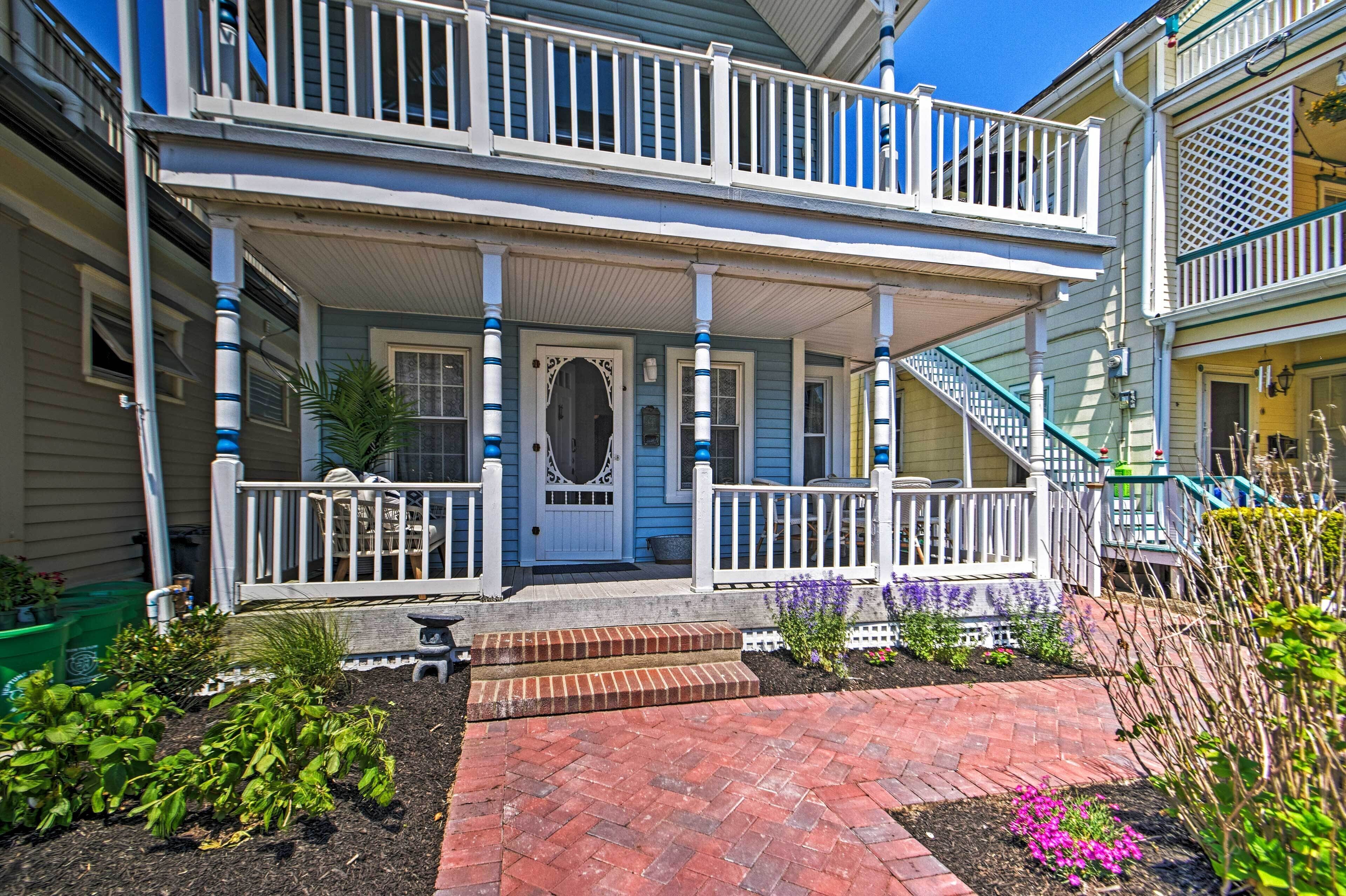 A two-story house with a porch, a front door, and a small garden area with plants and flowers.