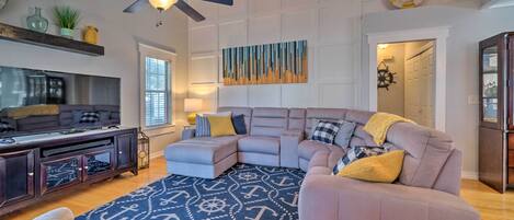 A modern living room with a sectional sofa, a ceiling fan, a flat-screen TV, and a decorative rug with nautical patterns.
